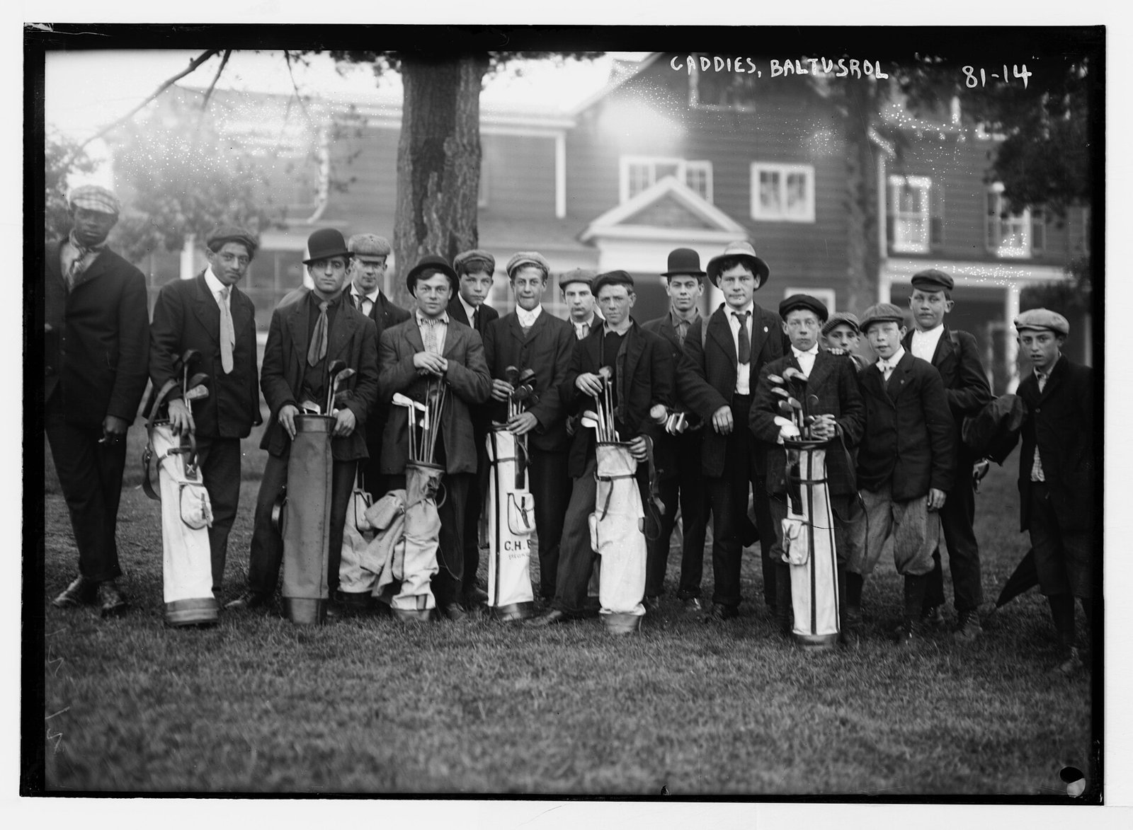 A row of caddies at Baltusrol in the early 20th century, each holding a narrow canvas pencil bag