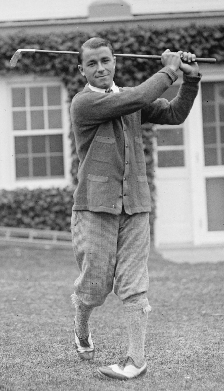 Gene Sarazen mid-swing in 1922, wearing plus fours, a cardigan, patterned knee socks and two-tone shoes